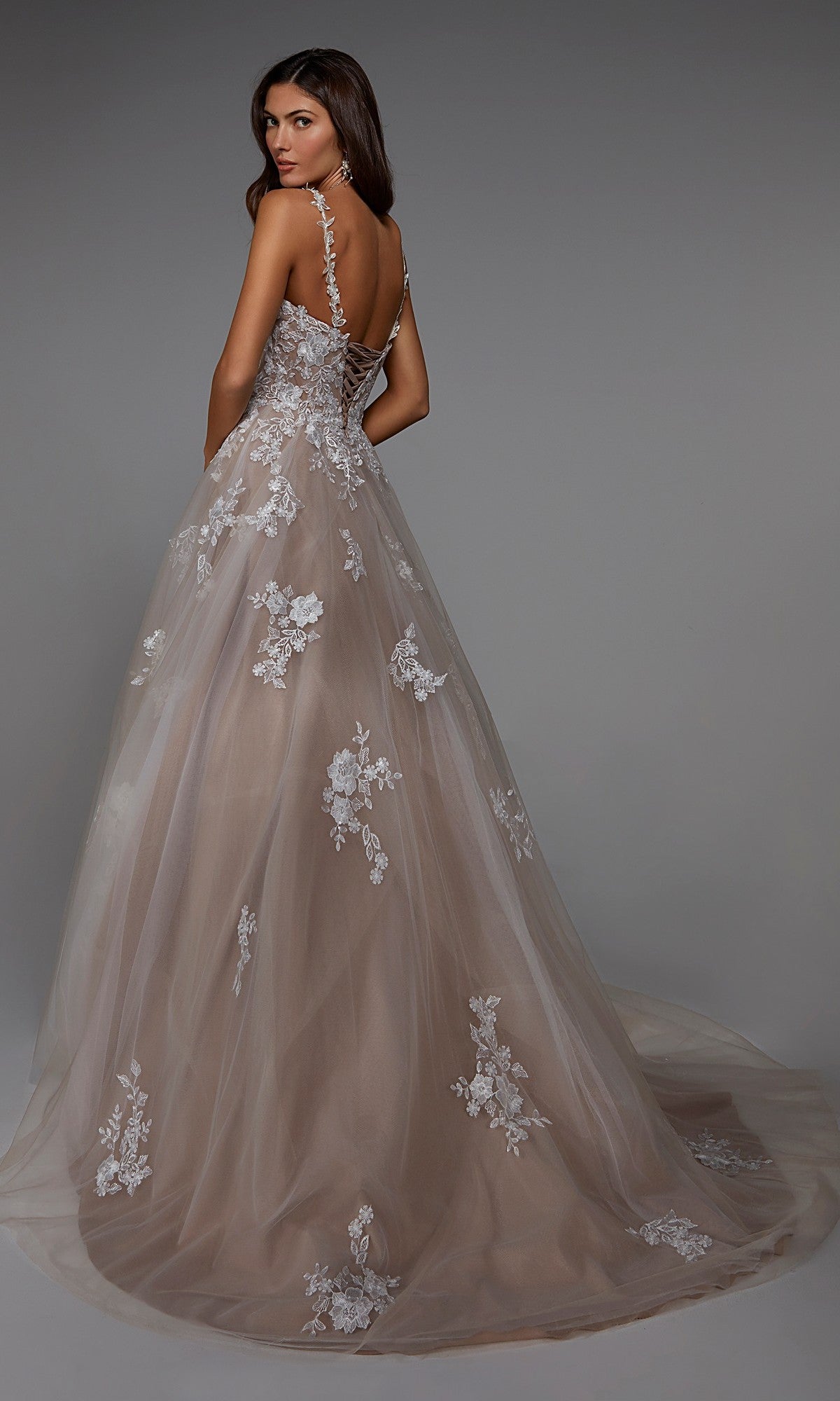 A woman poses gracefully in the Alyce 7043 long formal dress, featuring a beautiful A-line silhouette with floral lace appliqués and a tulle overlay, set against a simple gray background.